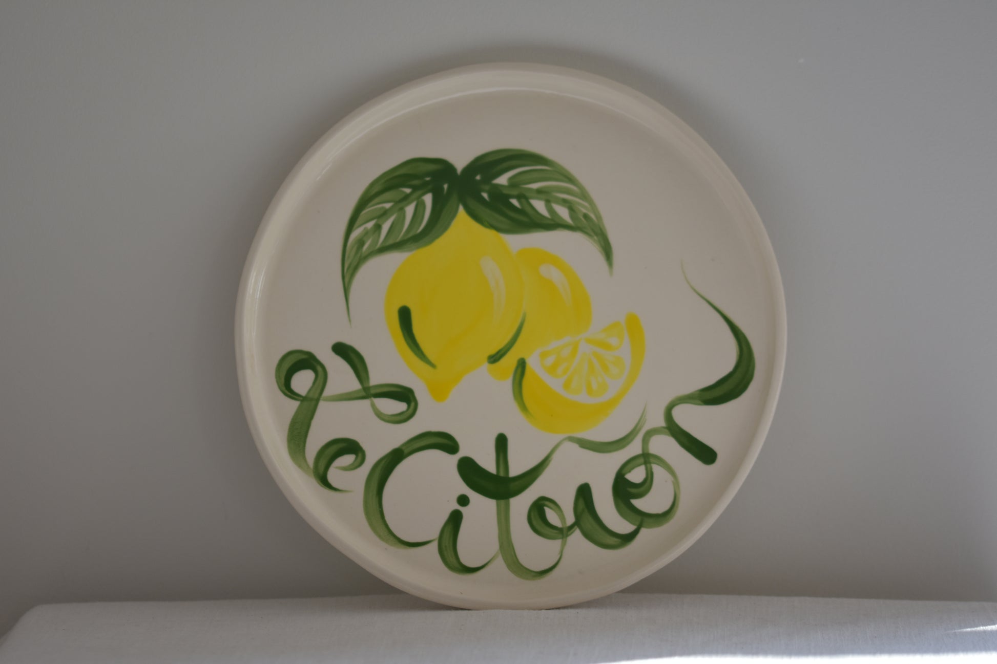 Le Crabe Le Citron ceramic plate with painted lemon and French writing, on a beige background.