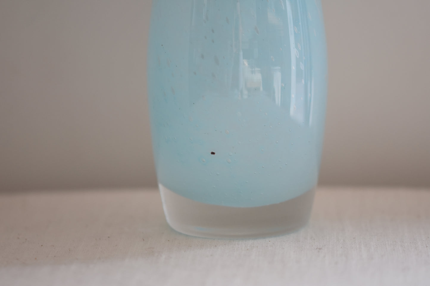 Close up of a vintage light blue glass vase on a beige background.