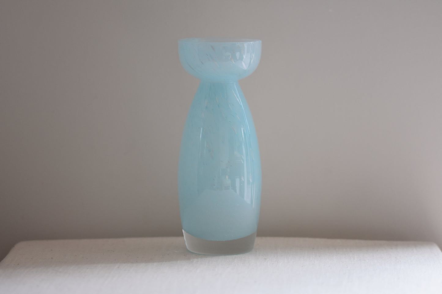 Vintage light blue glass vase on a beige background.