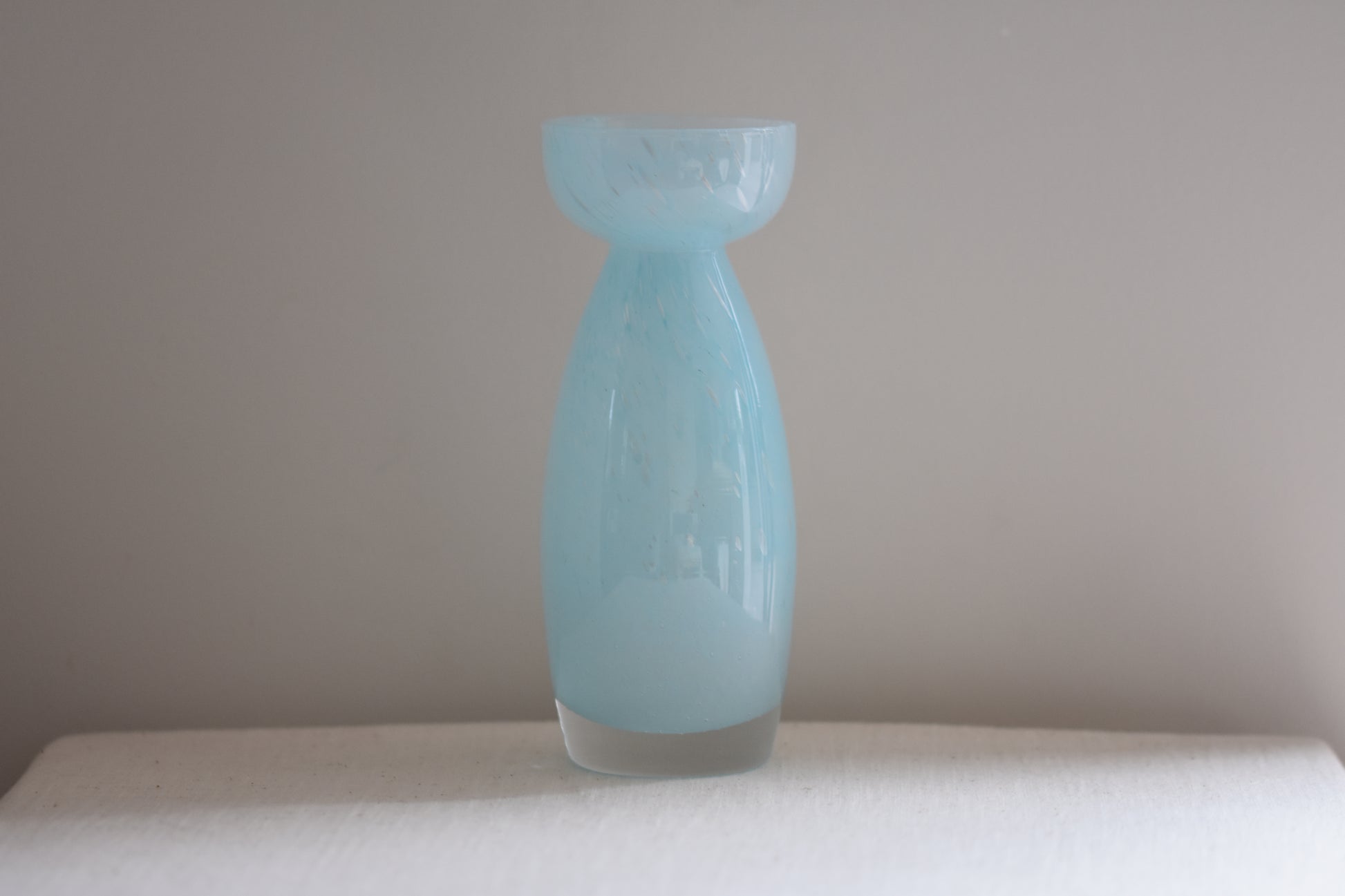 Vintage light blue glass vase on a beige background.