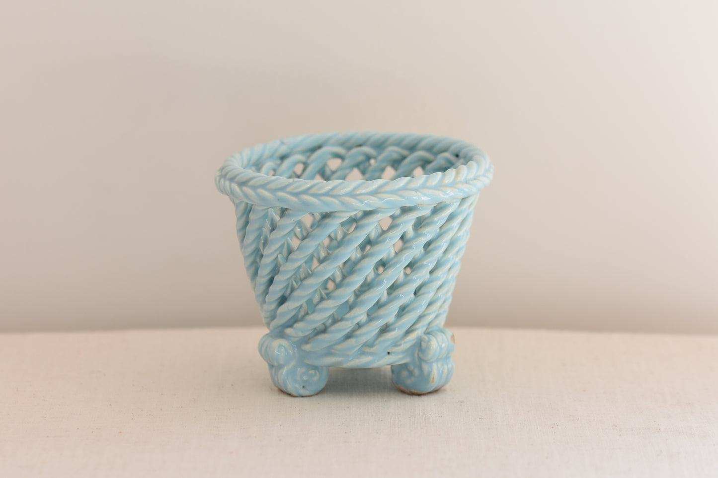 Vintage light blue woven ceramic pot on a beige background.