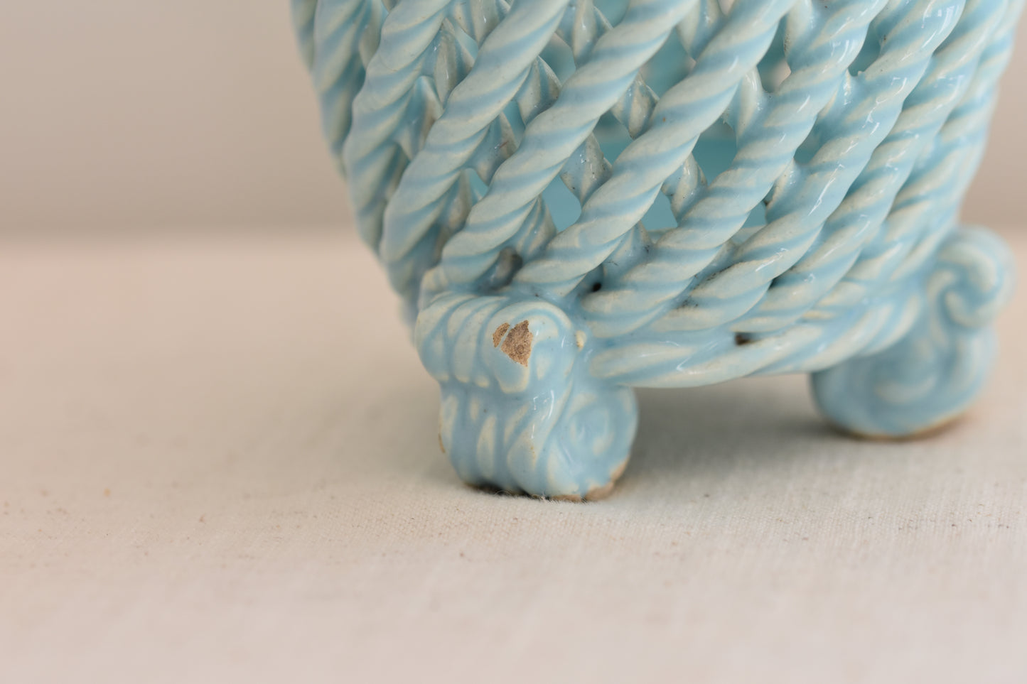 Close up of a vintage light blue woven ceramic pot on a beige background. 