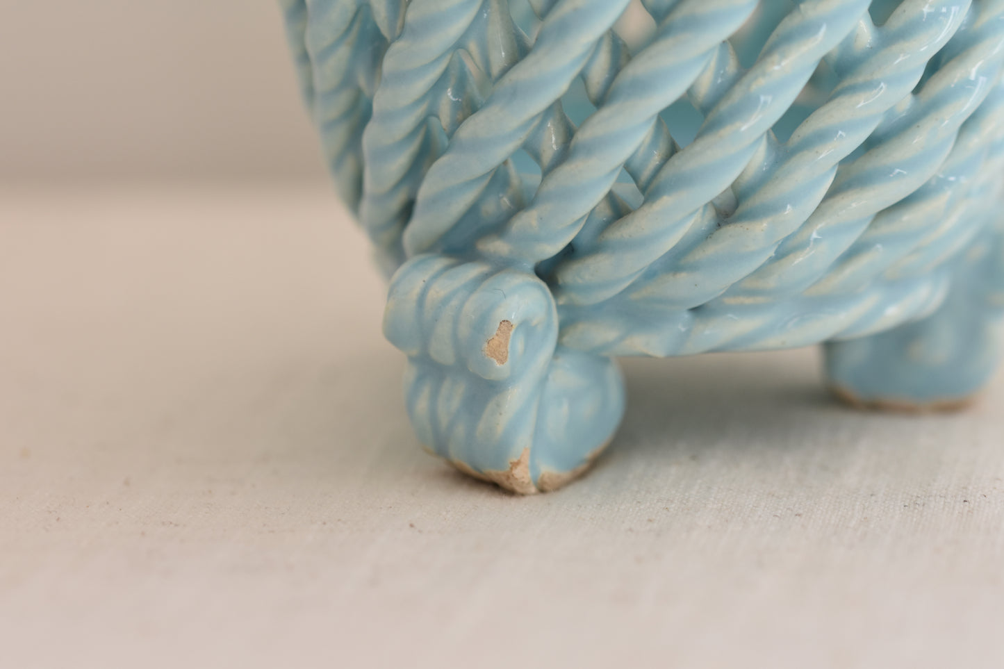 Close up of a vintage light blue woven ceramic pot on a beige background. 