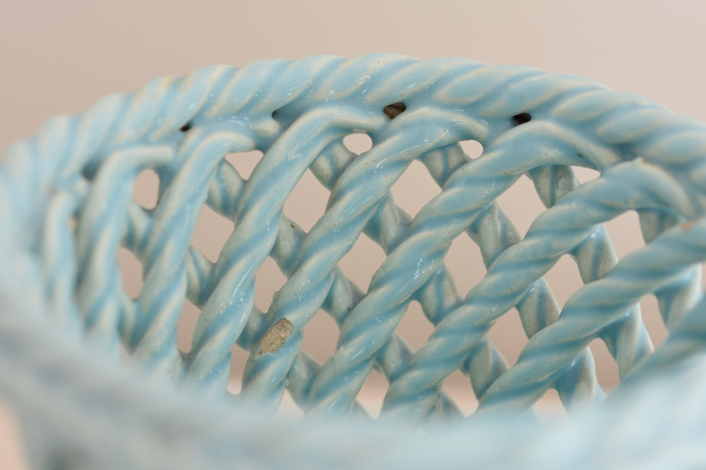 Close up of a vintage light blue woven ceramic pot on a beige background. 