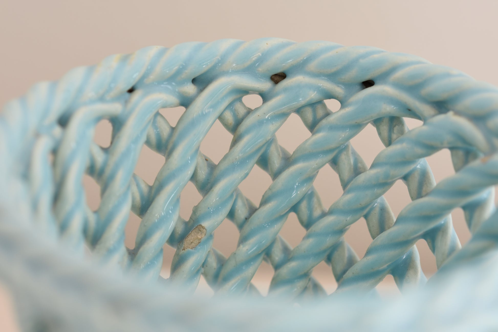 Close up of a vintage light blue woven ceramic pot on a beige background. 
