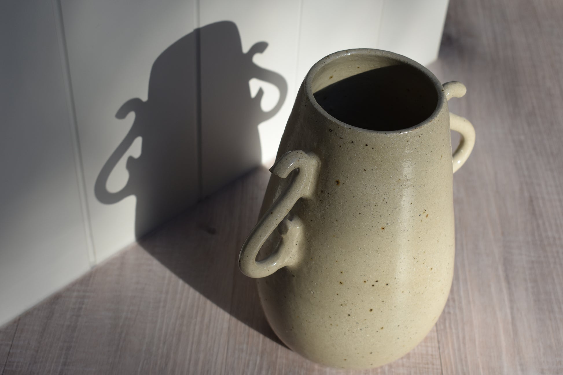 We Are Clay Curly Vase in flecked beige ceramic with curly handles and it's shadow.