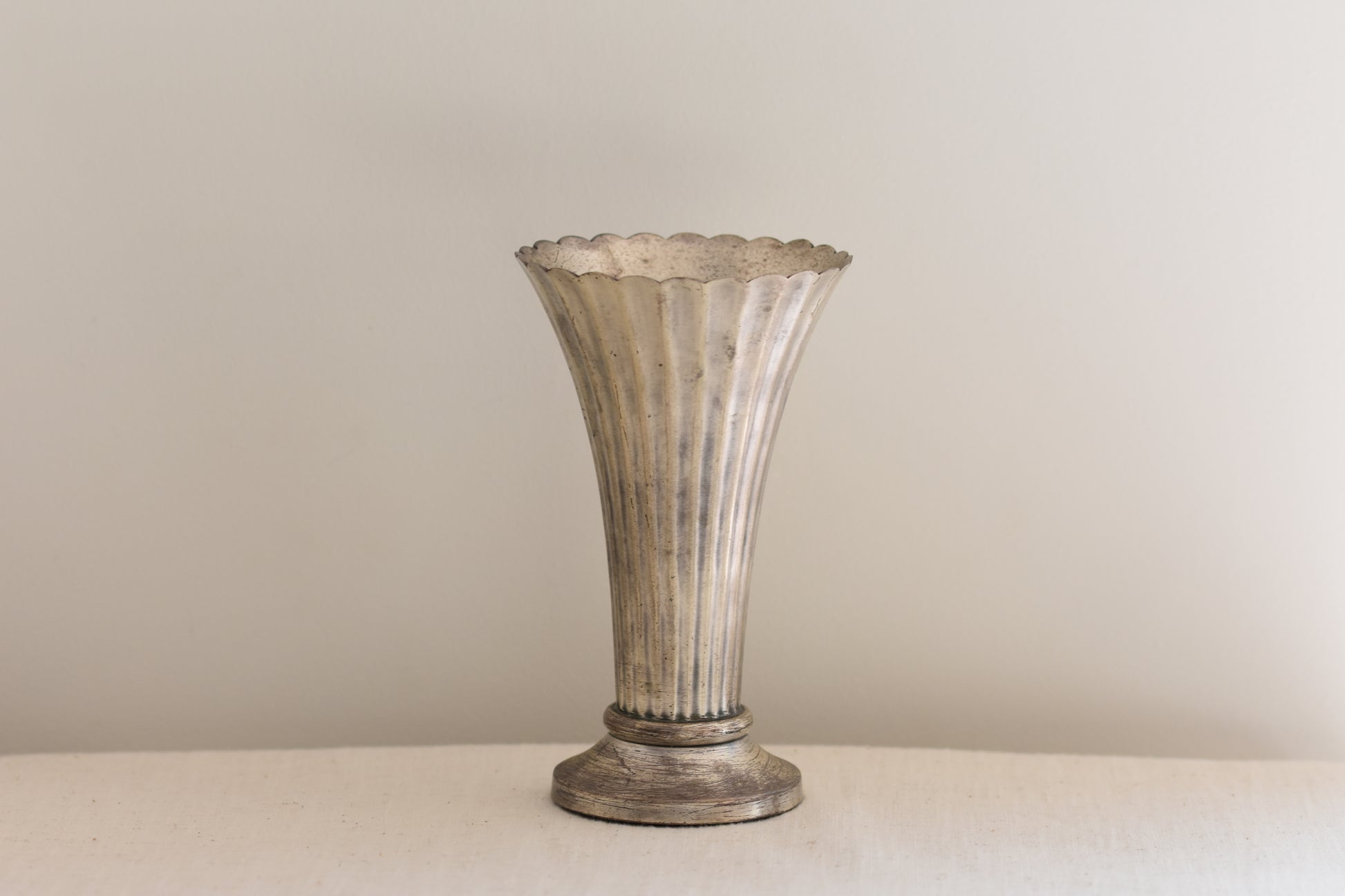 Vintage silver plated fluted vase on a beige background.