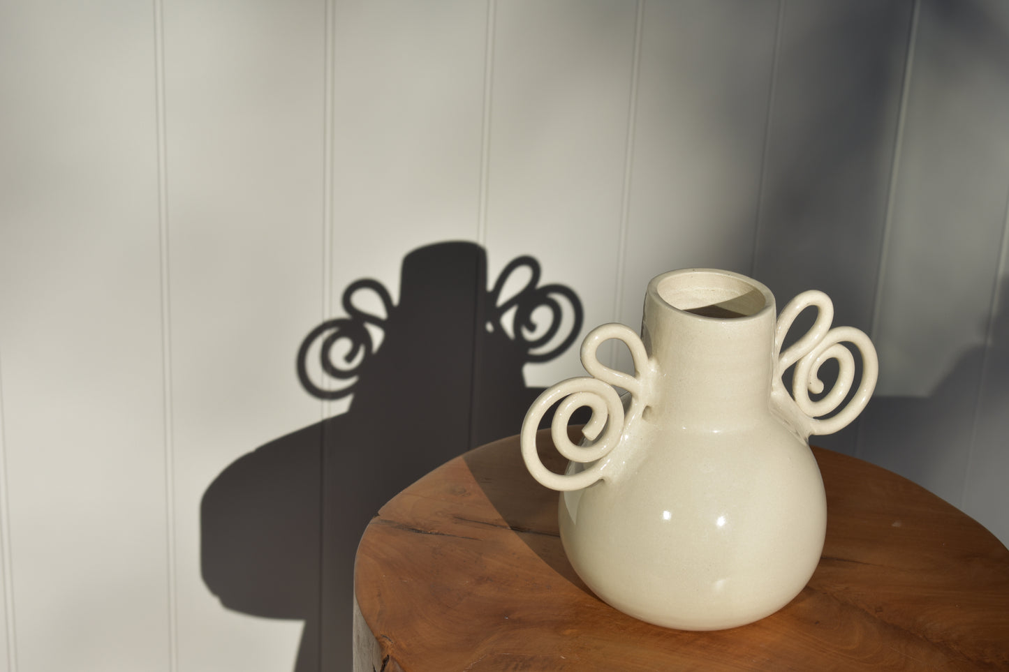 We Are Clay Pretzel Vase in white ceramic with spiral handles and it's shadow.