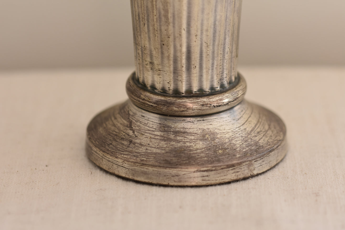 Close up of a vintage silver plated fluted vase on a beige background.