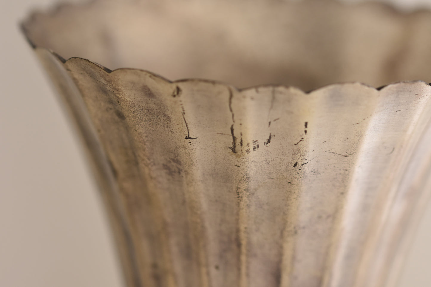 Close up of a vintage silver plated fluted vase on a beige background.