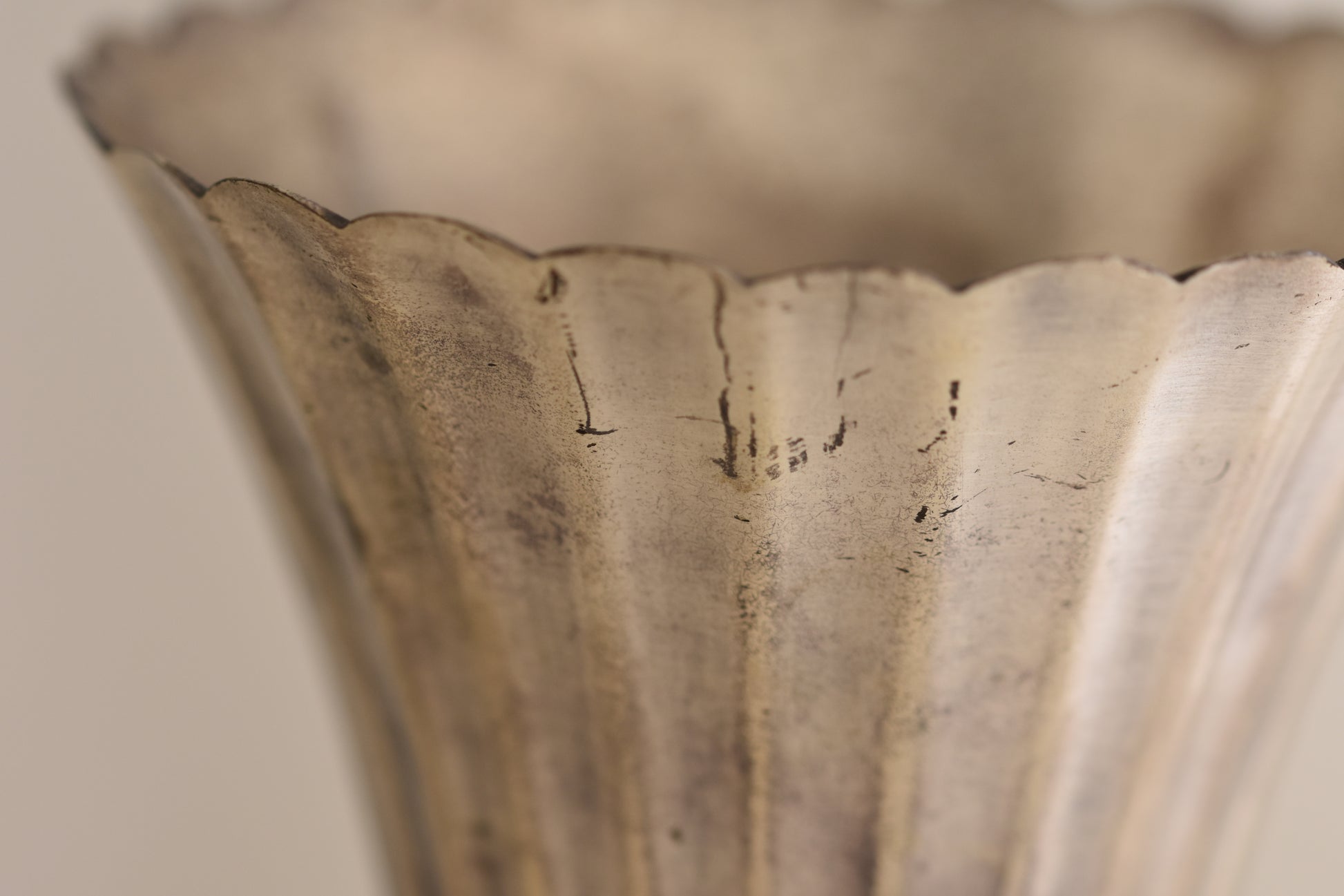 Close up of a vintage silver plated fluted vase on a beige background.