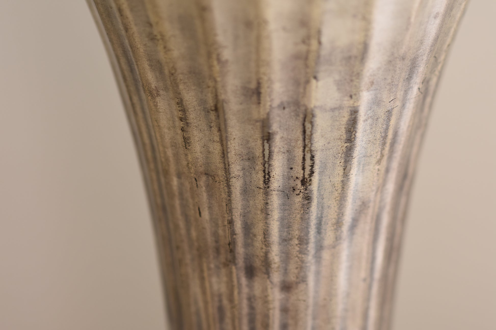 Close up of a vintage silver plated fluted vase on a beige background.