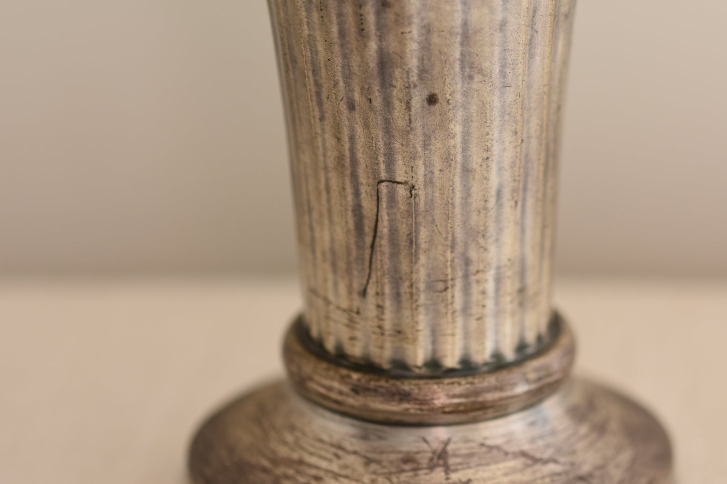 Close up of a vintage silver plated fluted vase on a beige background.