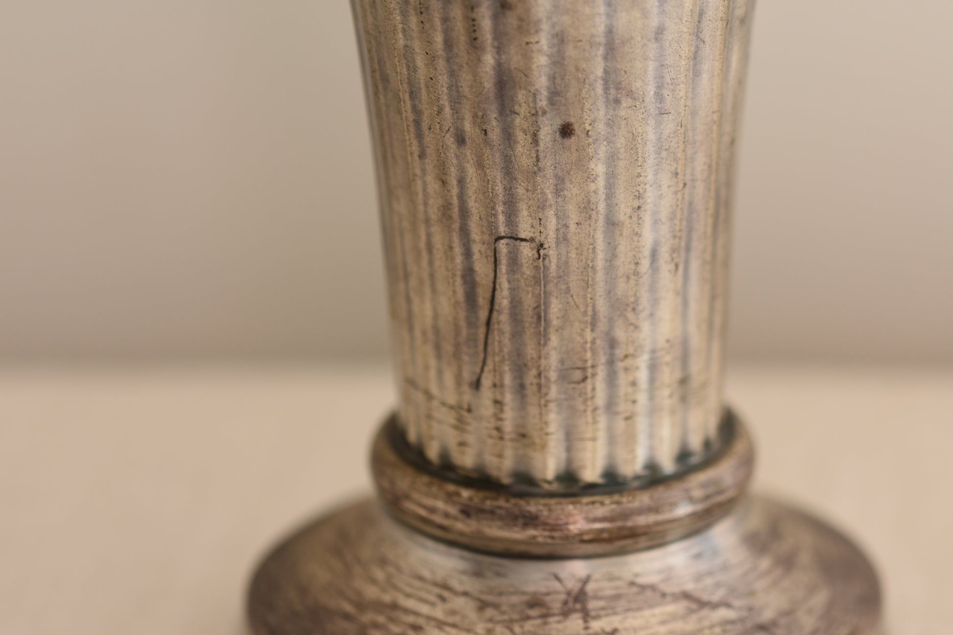 Close up of a vintage silver plated fluted vase on a beige background.