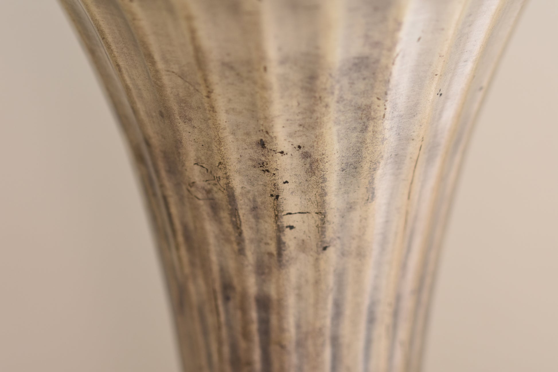 Close up of a vintage silver plated fluted vase on a beige background.