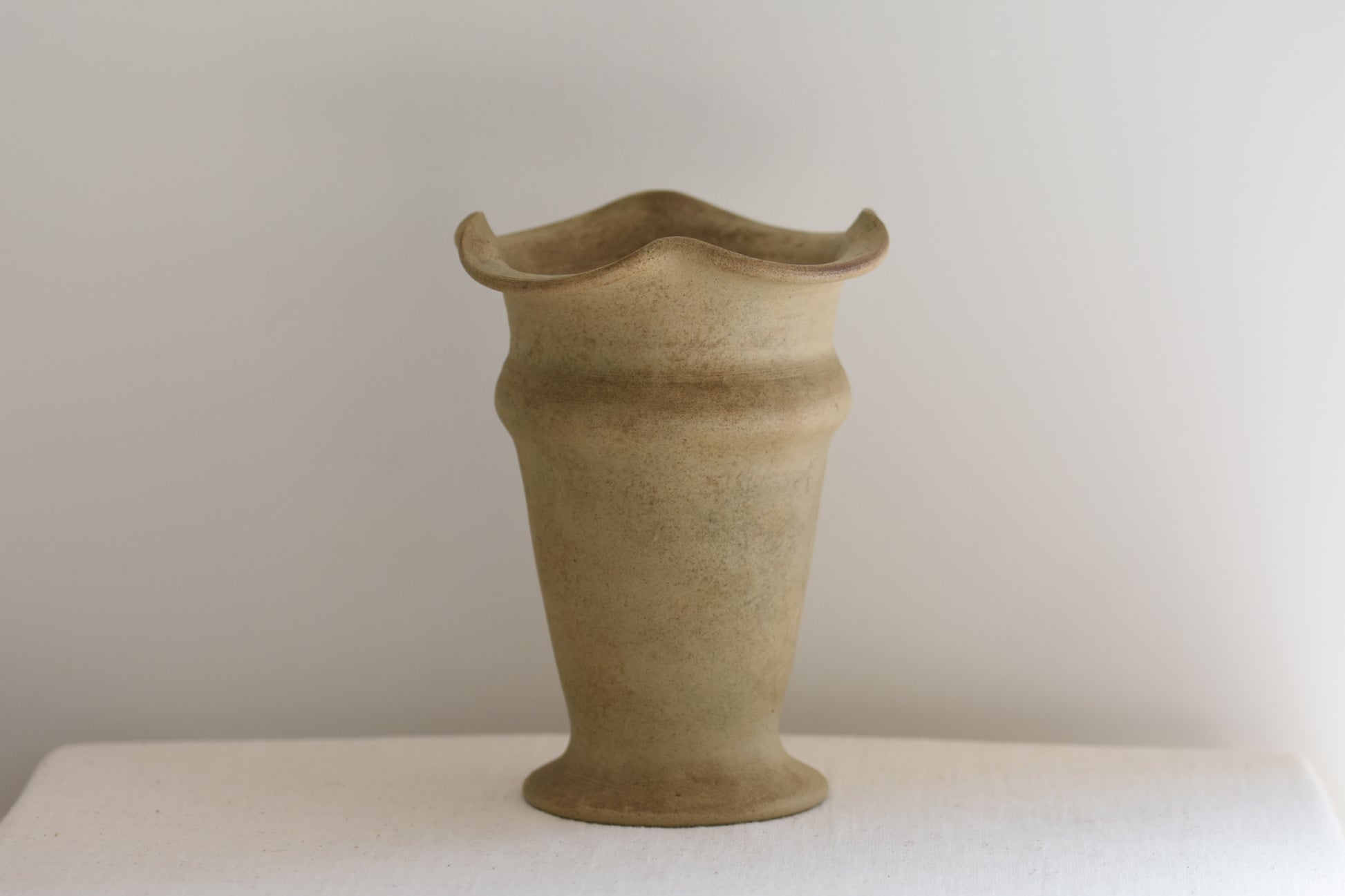Vintage Hillstonia beige stoneware vase with wavy rim on a beige background.