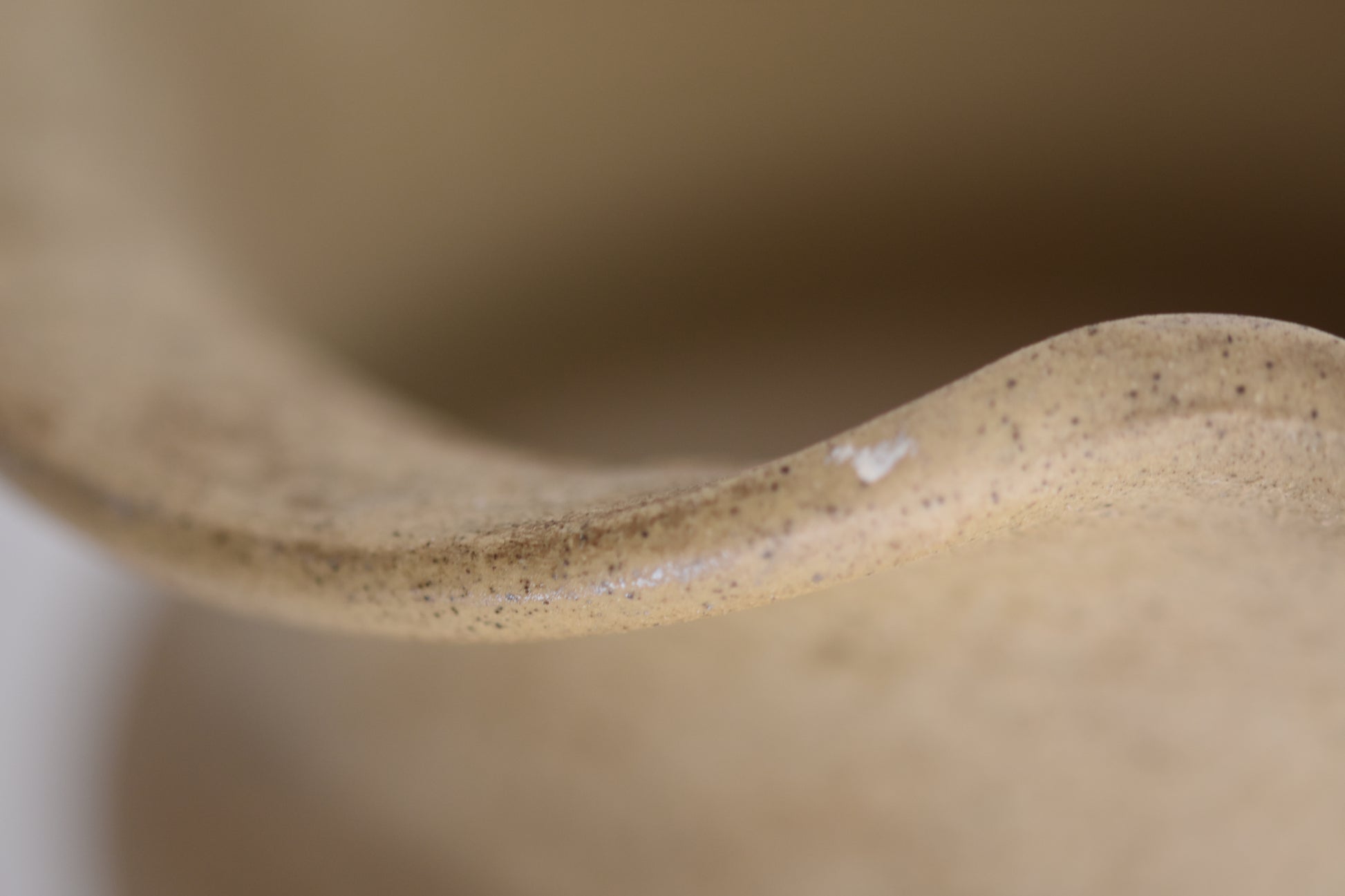 Close up of a vintage Hillstonia beige stoneware vase with wavy rim on a beige background.