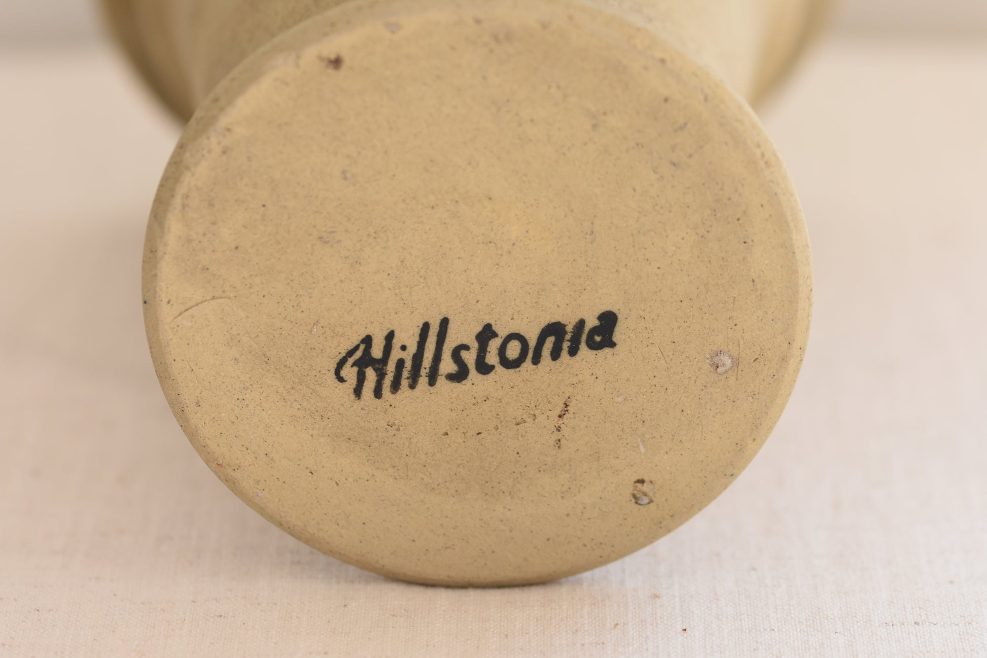 Close up of vintage Hillstonia beige stoneware vase base on a beige background.