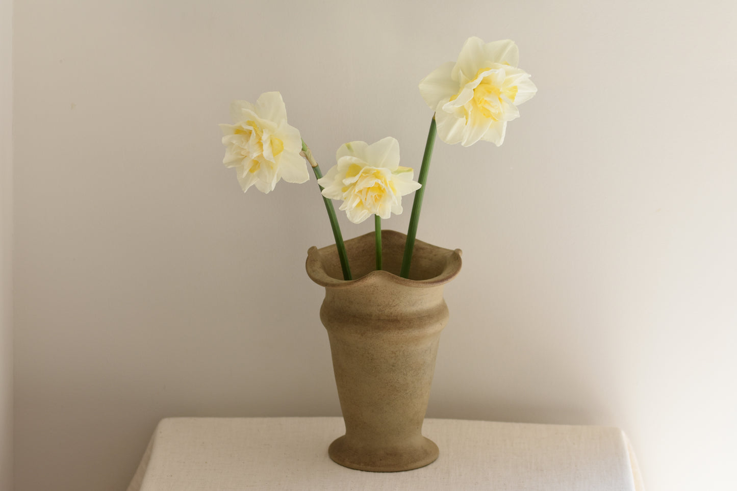 Vintage Hillstonia beige stoneware vase with wavy rim containing daffodils on a beige background.