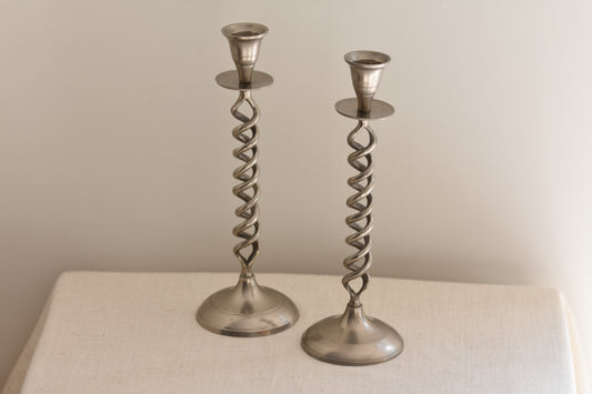 Pair of vintage silver tone metal twist candlesticks on a beige background.