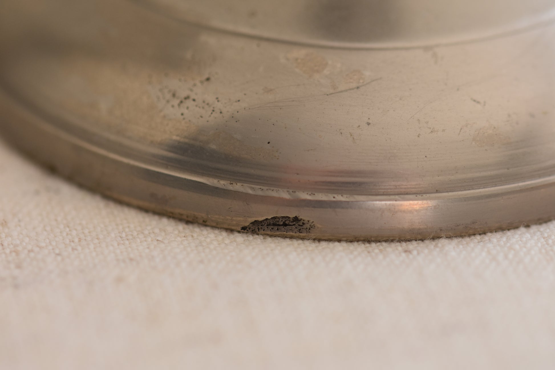 Close up of base of a vintage silver tone metal twist candlestick on a beige background.