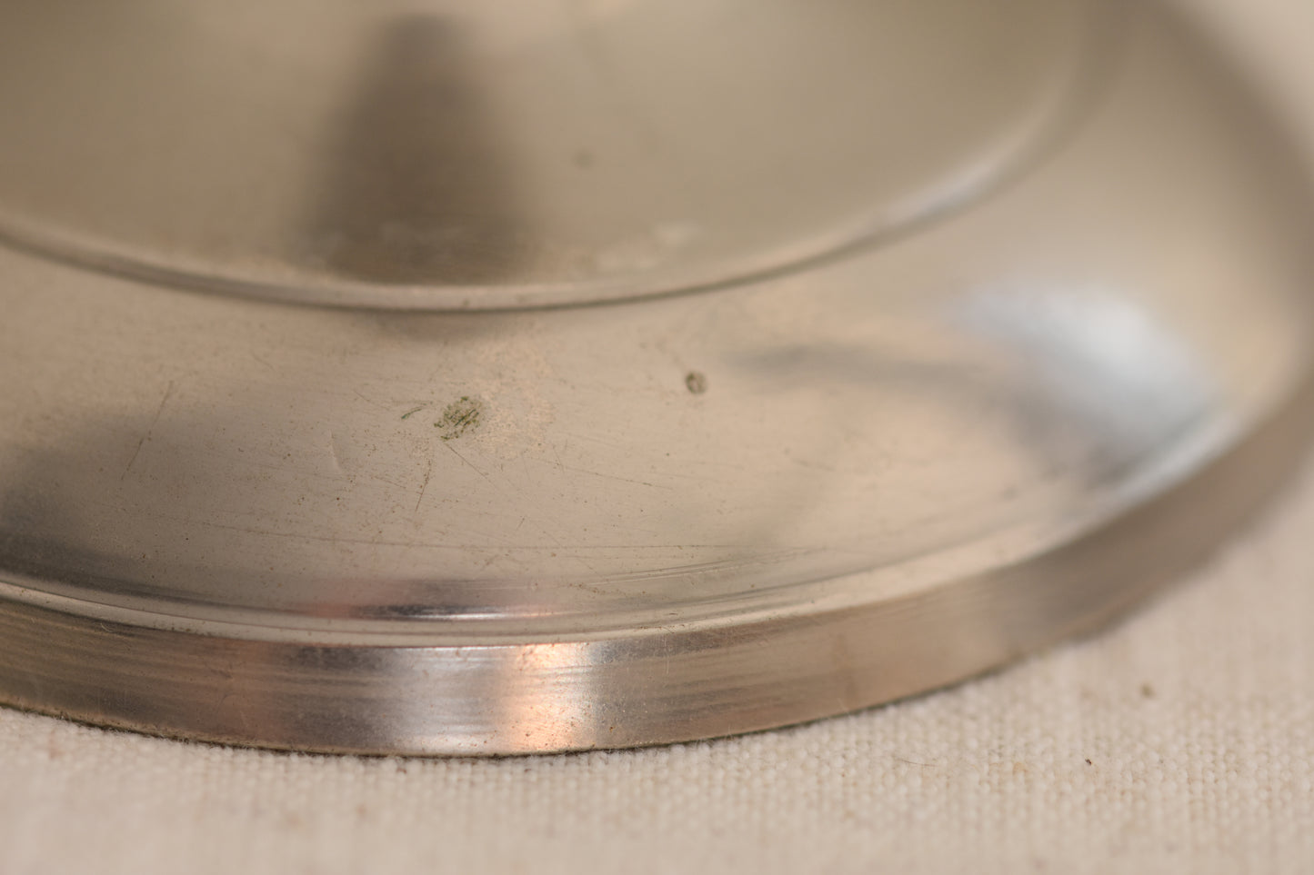 Close up of base of a vintage silver tone metal twist candlestick on a beige background.