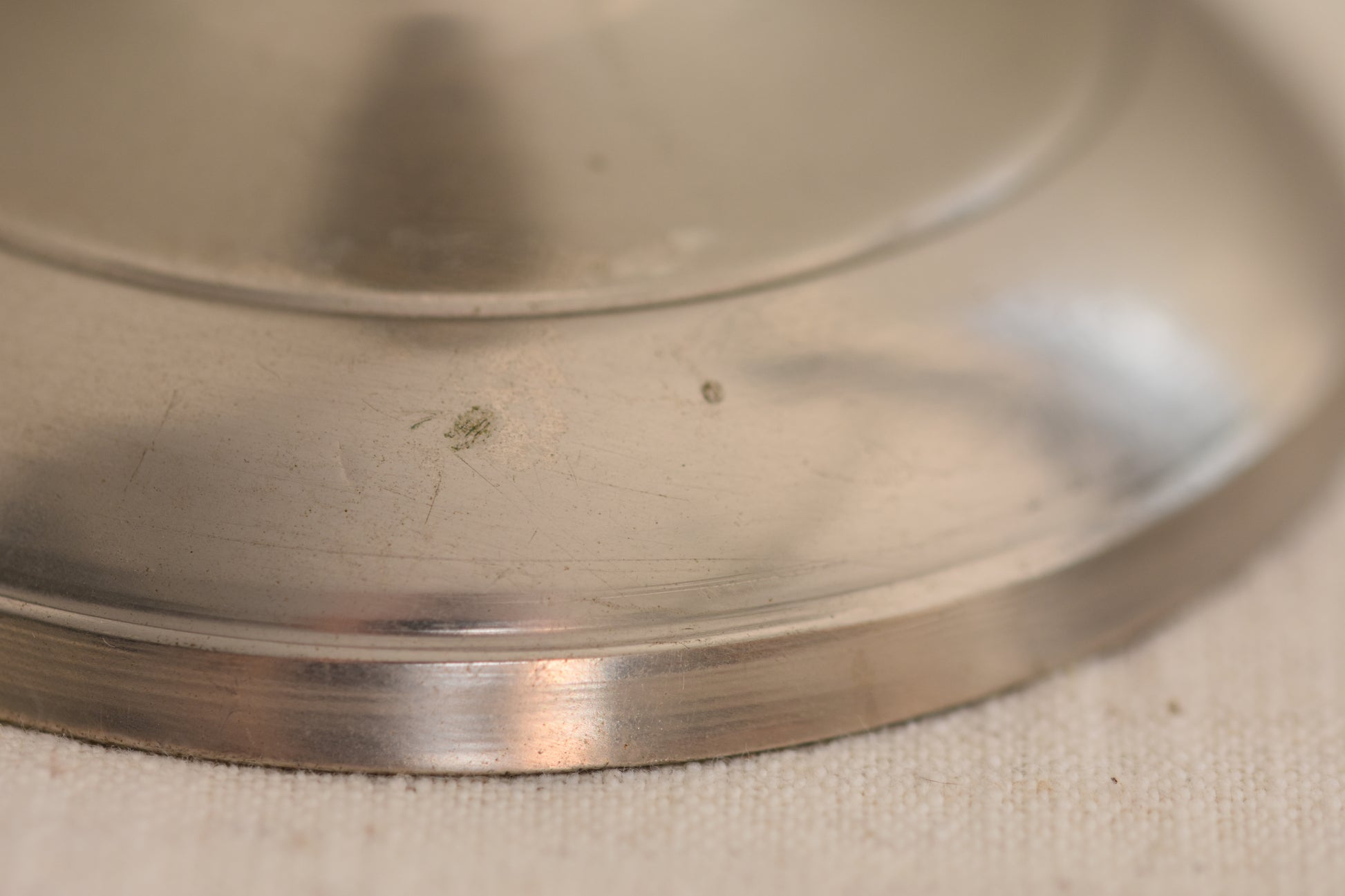 Close up of base of a vintage silver tone metal twist candlestick on a beige background.