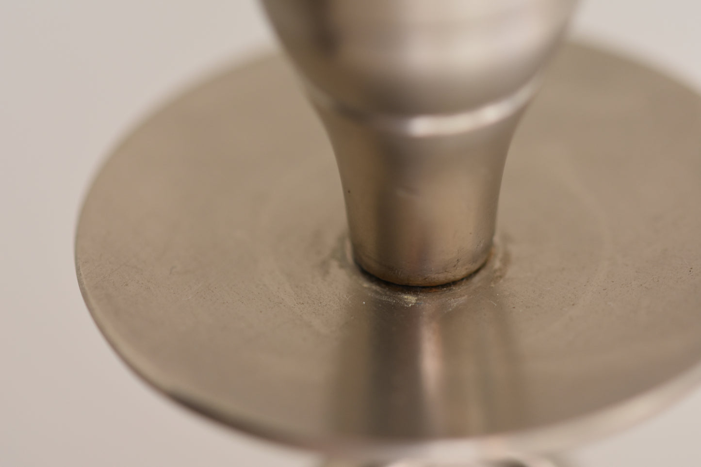Close up of a vintage silver tone metal twist candlestick on a beige background.