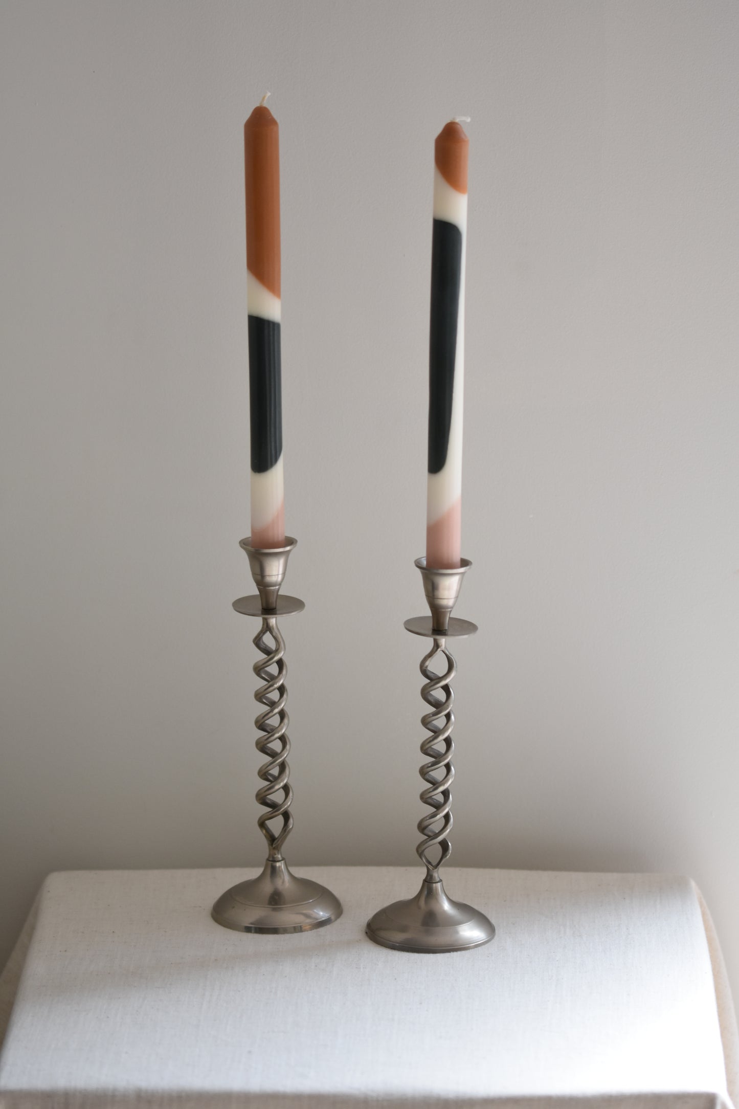 Pair of vintage silver tone metal twist candlesticks containing patterned candles, on a beige background.