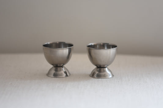 Pair of vintage Danish stainless steel egg cups on a beige background.