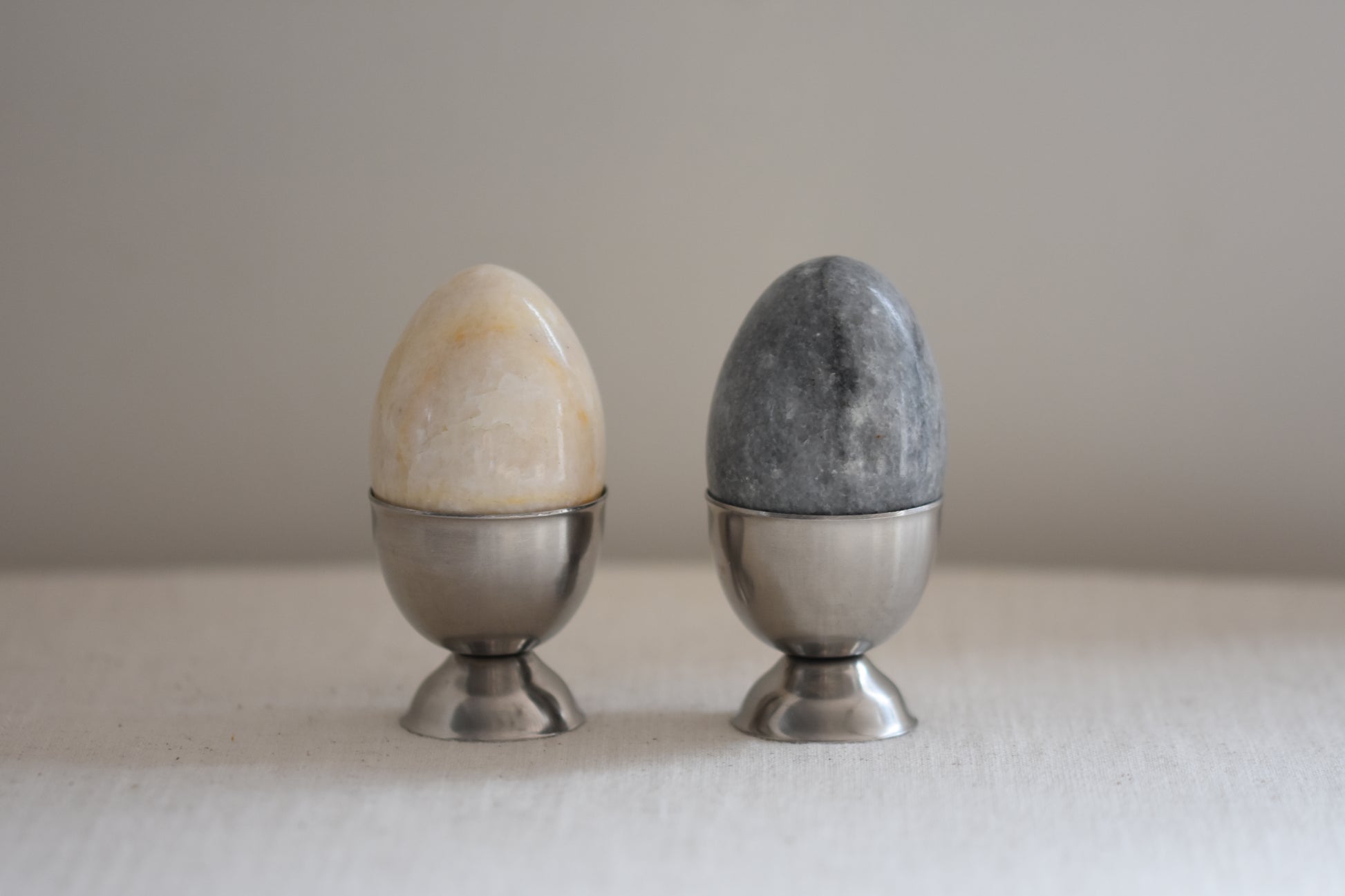 Pair of vintage Danish stainless steel egg cups holding stone eggs, on a beige background.