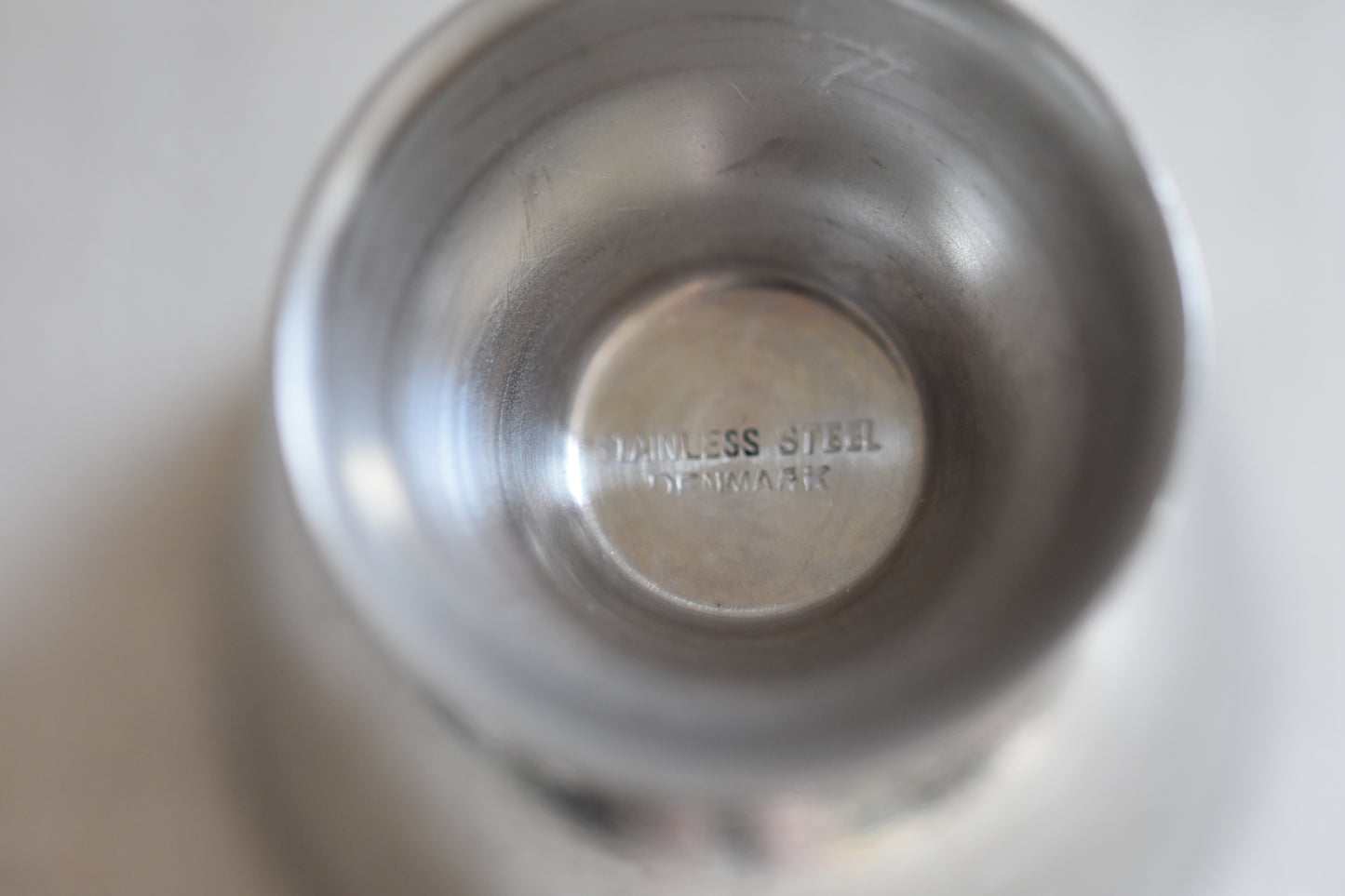 Close up of base of a vintage Danish stainless steel egg cup, on a beige background.