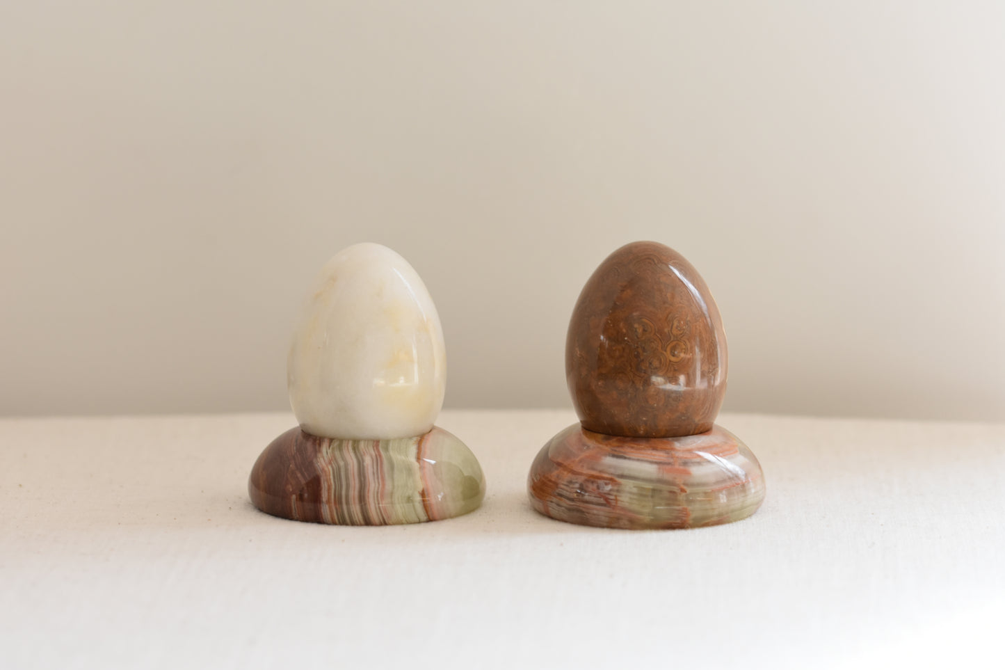 Pair of vintage green and brown onyx egg holders containing stone eggs, on a beige background.