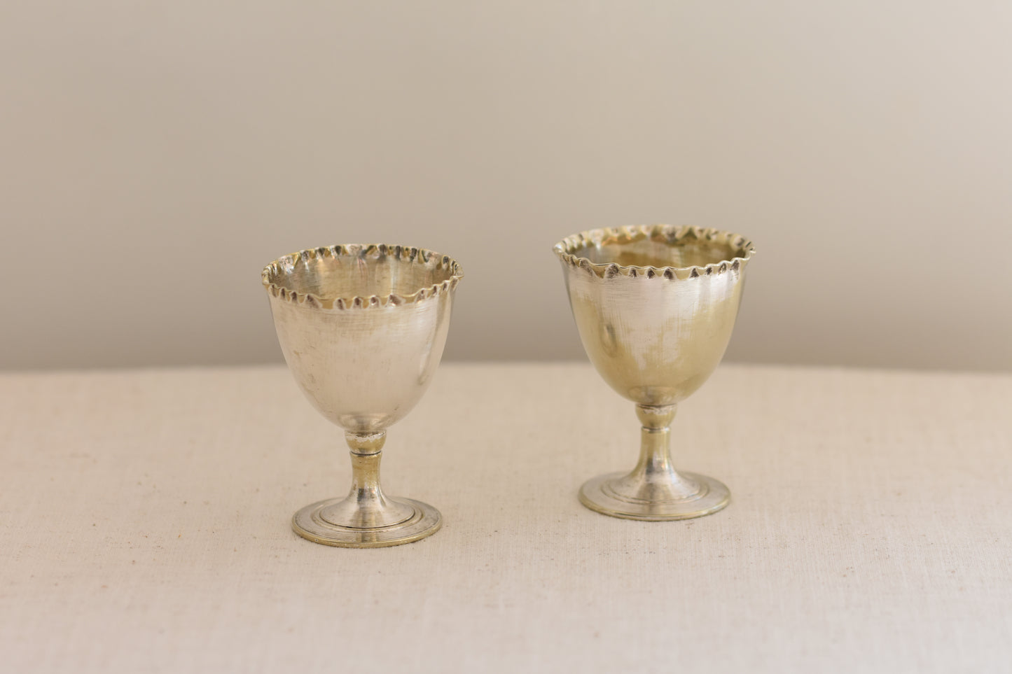 Pair of vintage silver plated egg cups with crimped rims on a beige background.
