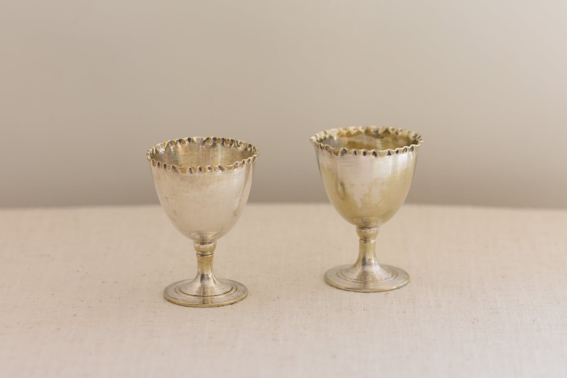 Pair of vintage silver plated egg cups with crimped rims on a beige background.