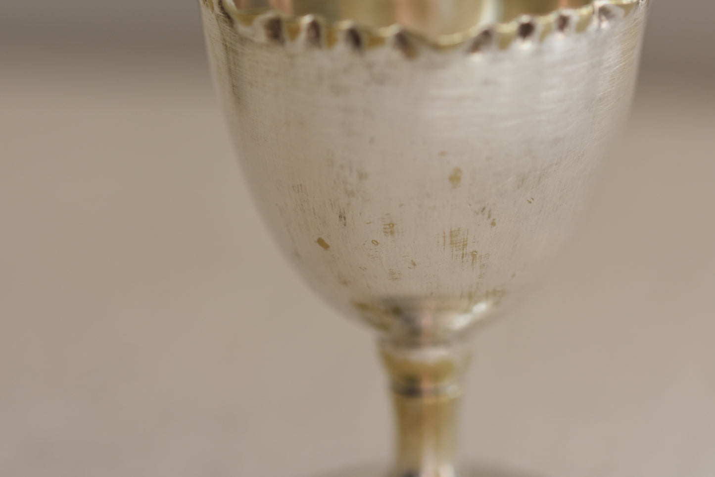 Close up of a vintage silver plated egg cup with crimped rim on a beige background.