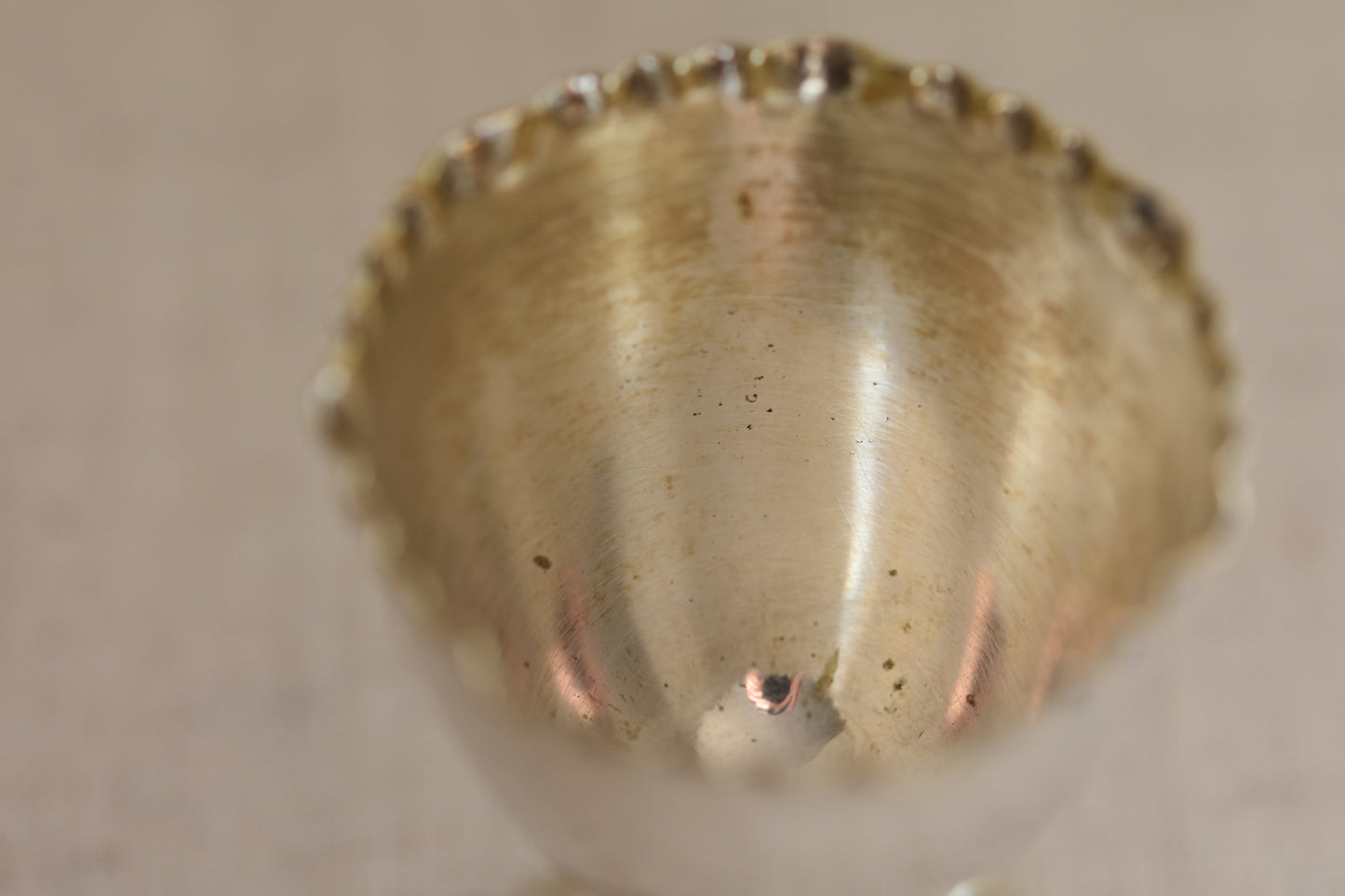 Close up of the inside of a vintage silver plated egg cup with crimped rim on a beige background.