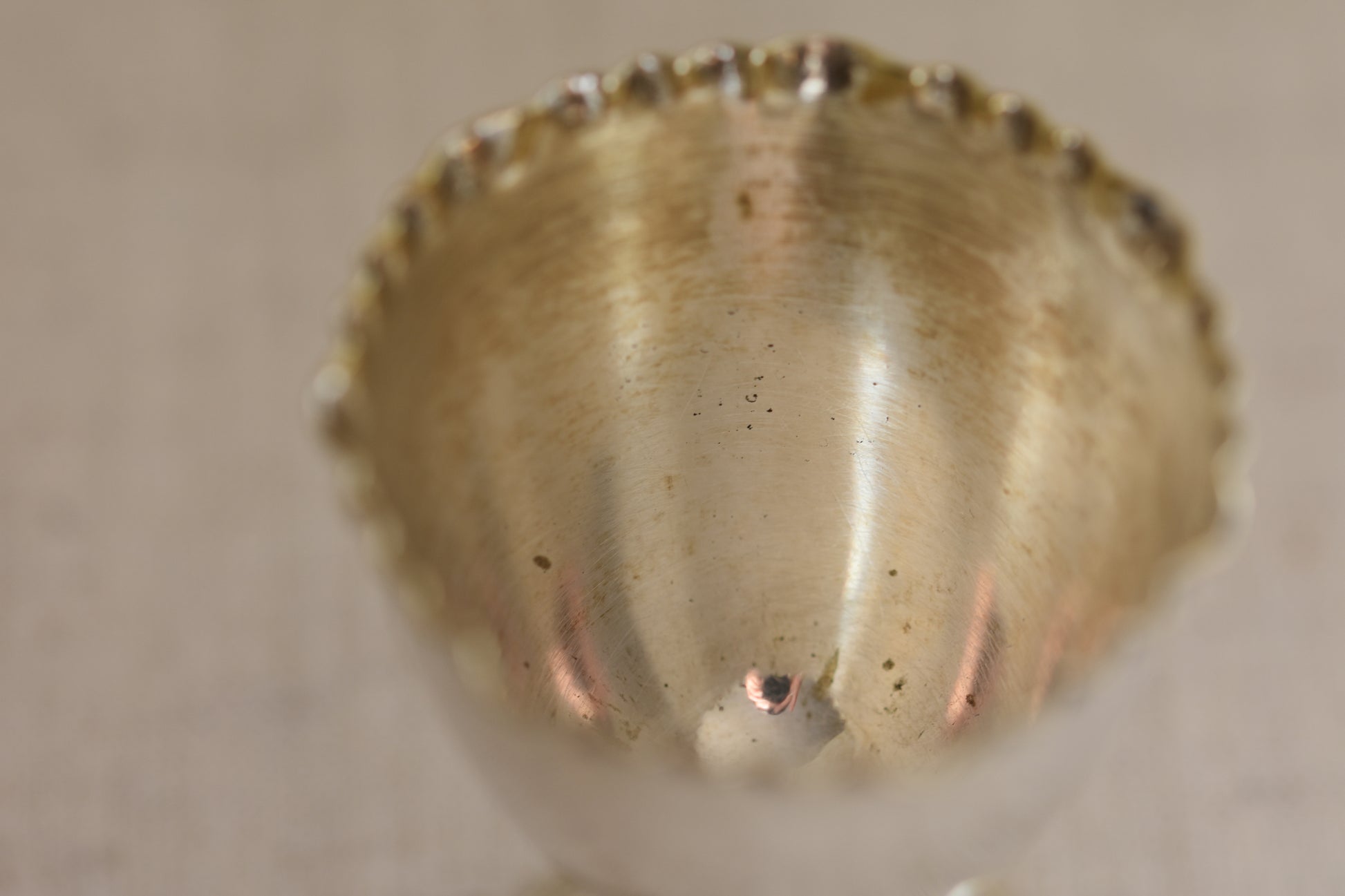 Close up of the inside of a vintage silver plated egg cup with crimped rim on a beige background.