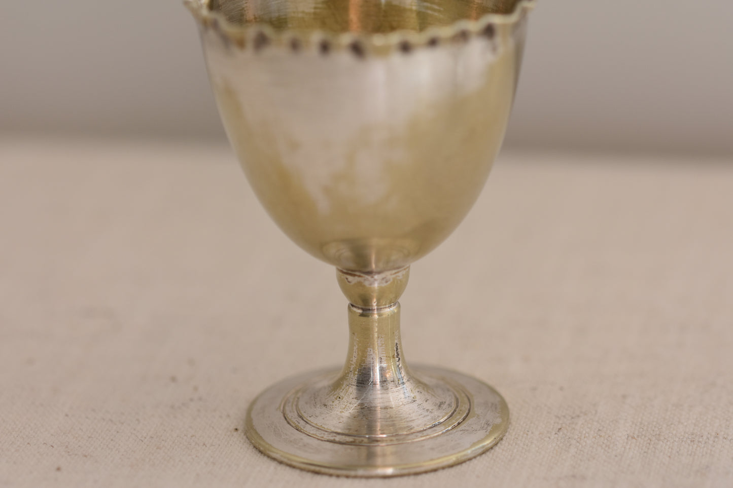 Close up of a vintage silver plated egg cup with crimped rim on a beige background.