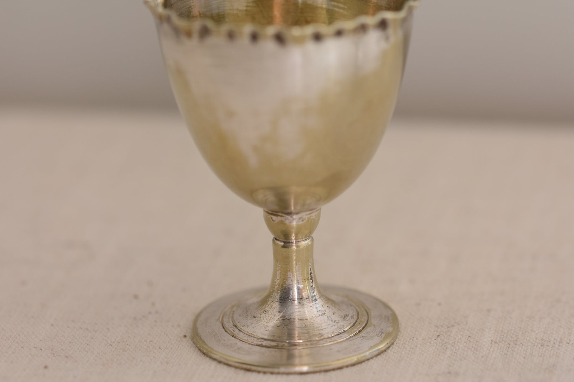 Close up of a vintage silver plated egg cup with crimped rim on a beige background.