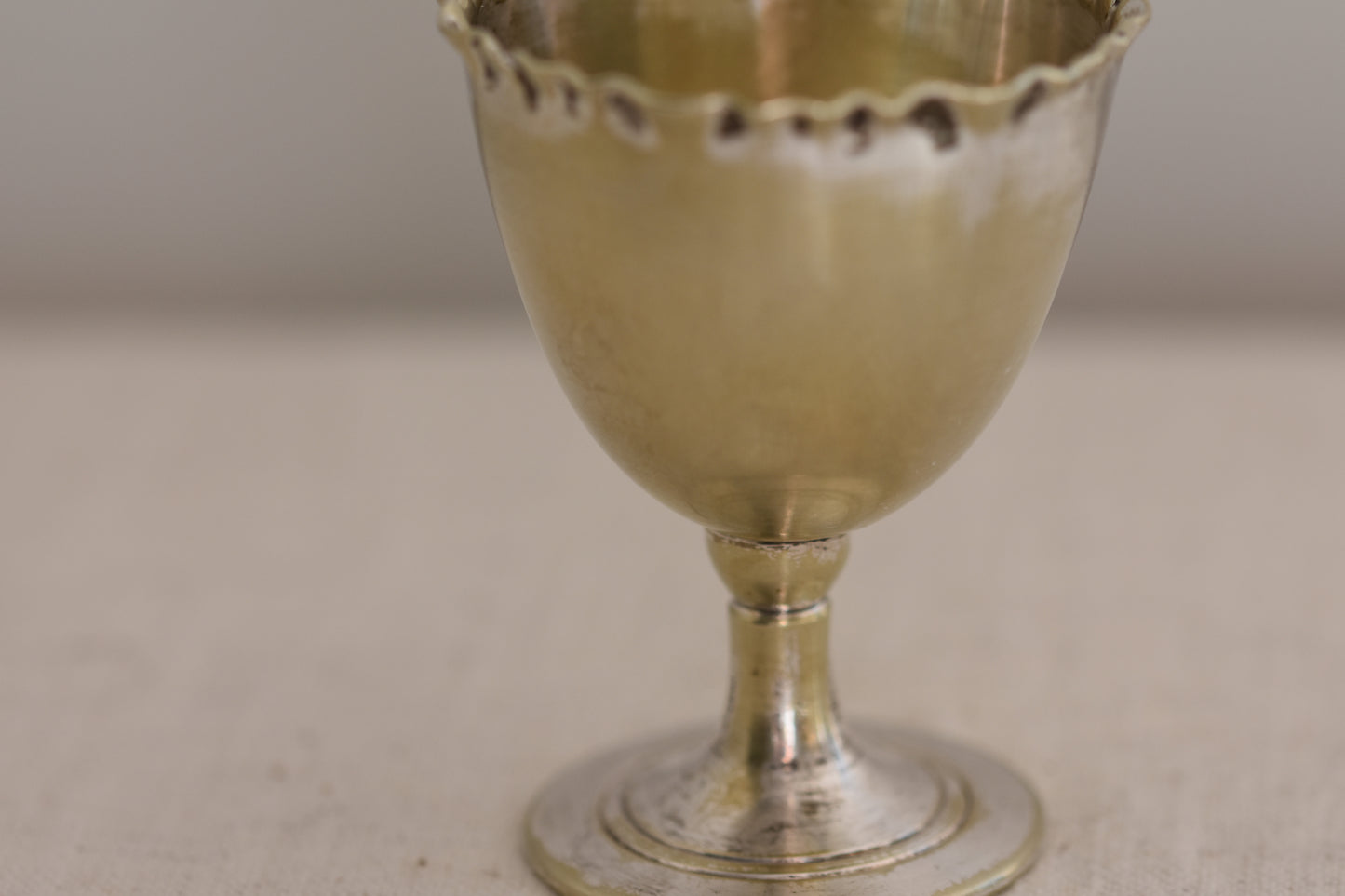 Close up of a vintage silver plated egg cup with crimped rim on a beige background.