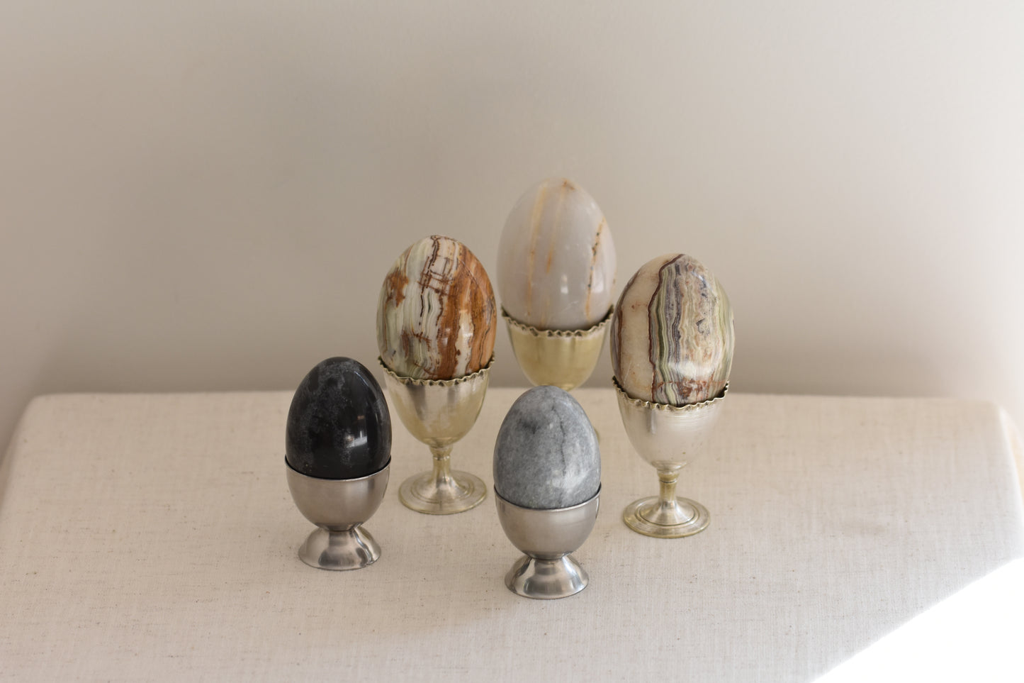 Silver egg cups containing five vintage stone eggs on a beige background.