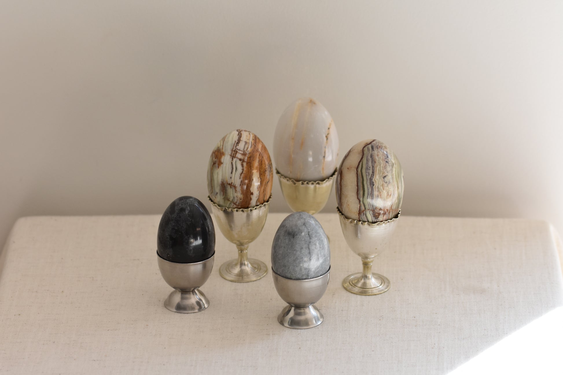 Silver egg cups containing five vintage stone eggs on a beige background.