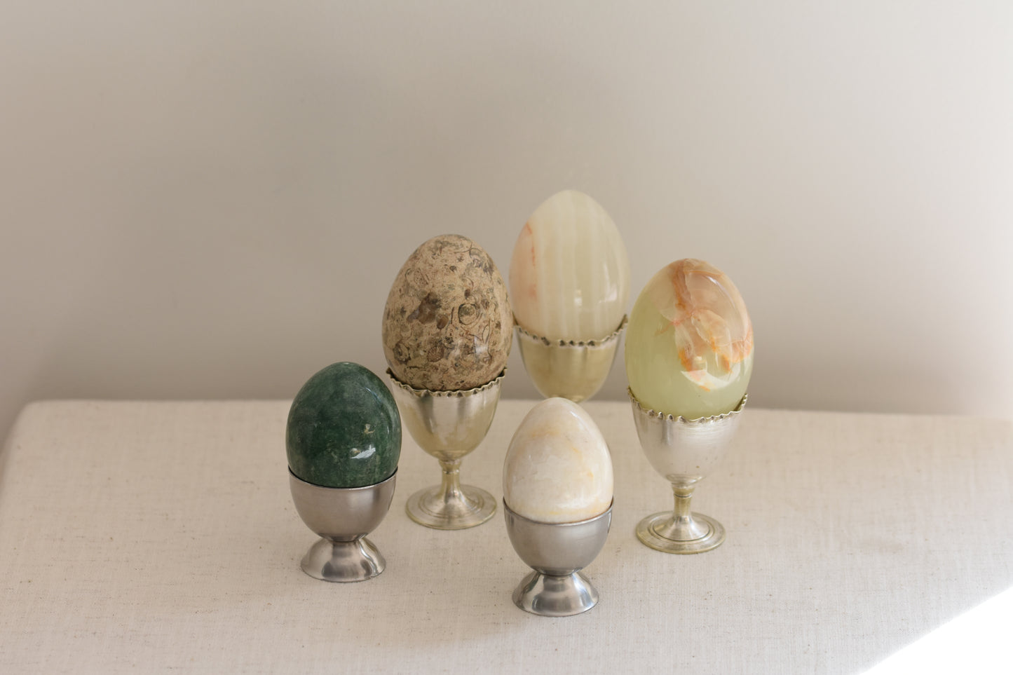 Silver egg cups containing five vintage stone eggs on a beige background.