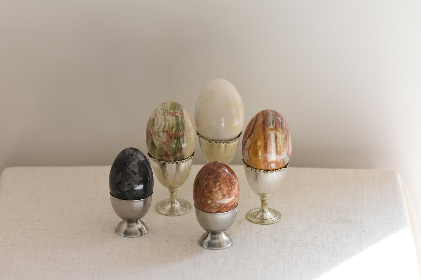 Silver egg cups containing five vintage stone eggs on a beige background.