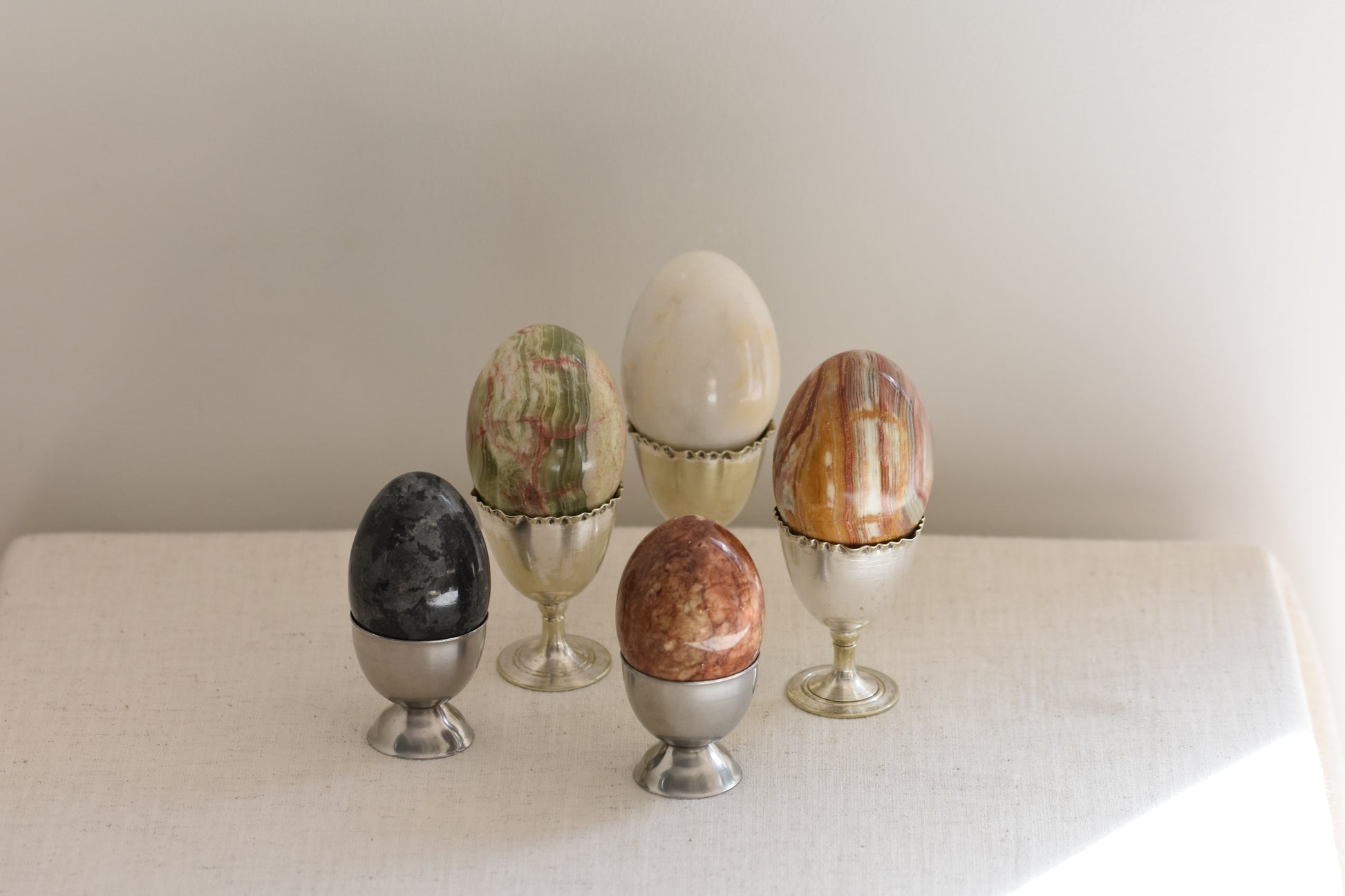 Silver egg cups containing five vintage stone eggs on a beige background.