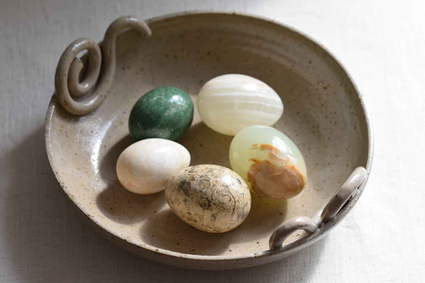 Ceramic bowl containing five vintage stone eggs on a beige background.