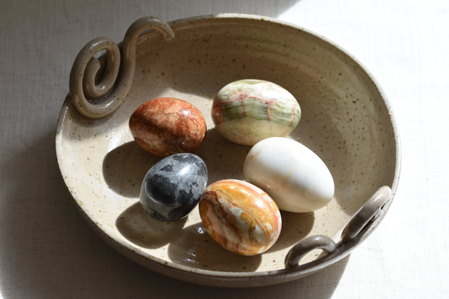 Ceramic bowl containing five vintage stone eggs on a beige background.