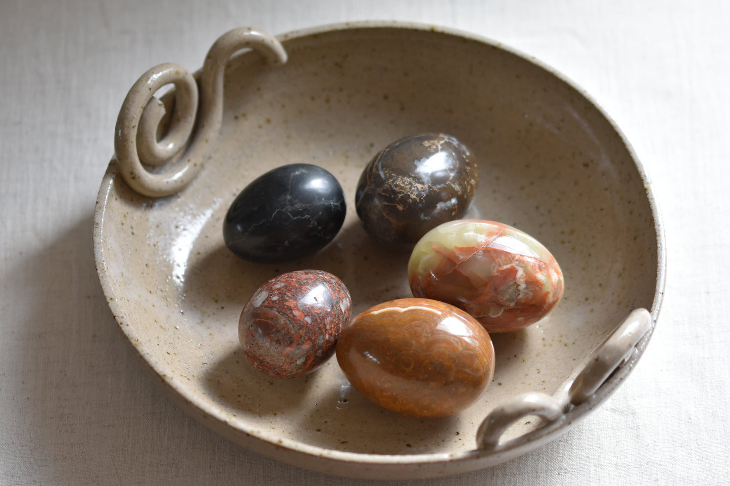 Ceramic bowl containing five vintage stone eggs on a beige background.