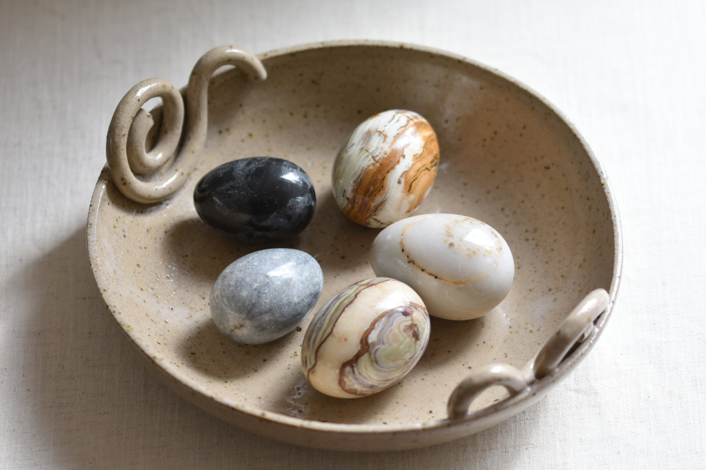 Ceramic bowl containing five vintage stone eggs on a beige background.